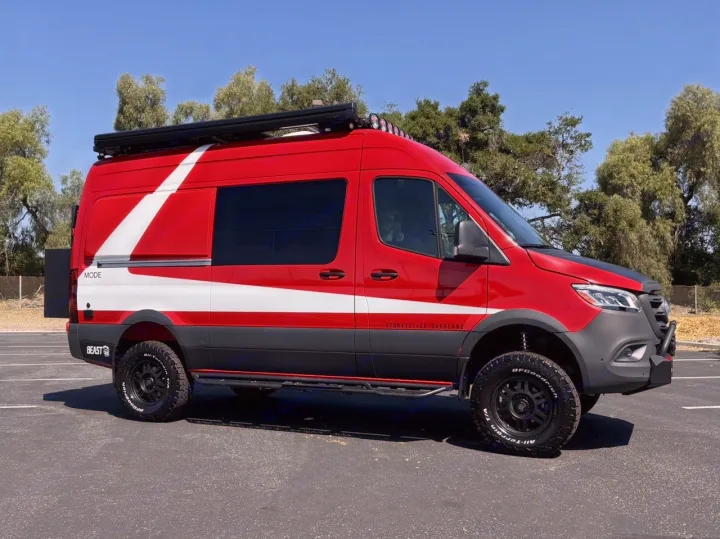 A bold red and white Storyteller Overland adventure van, ready for your next RV rental. Features include off-road tires and roof lights.. Storyteller Overland Beast Mode AWD 2024