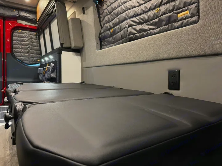 Explore this RV rental's cozy interior: modular black seating/bed, power outlet, insulated windows, ideal for mobile adventures.. Storyteller Overland Beast Mode AWD 2024