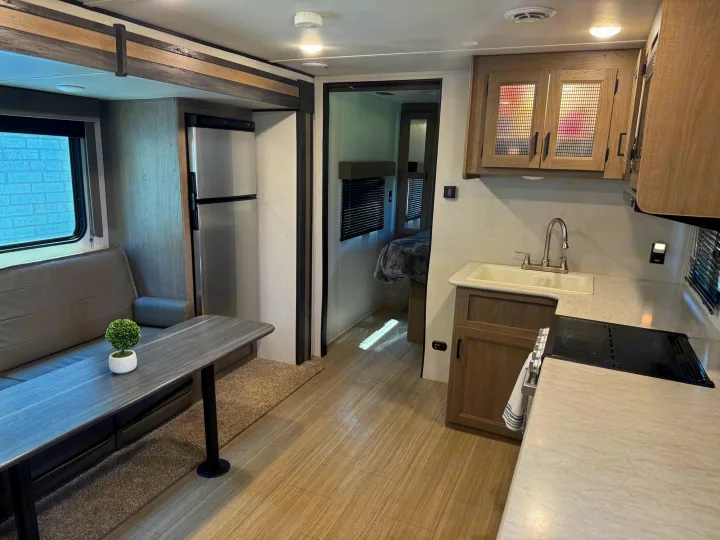 Inside this RV rental: modern kitchen, cozy living space with sofa & table, and a private bedroom visible through the doorway.. Keystone RV Hideout 2021