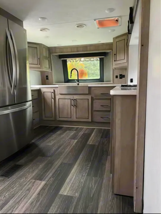 Modern RV rental kitchen featuring gray cabinets, stainless steel appliances, and dark wood-look flooring.. Heartland RVs Big Country 2021