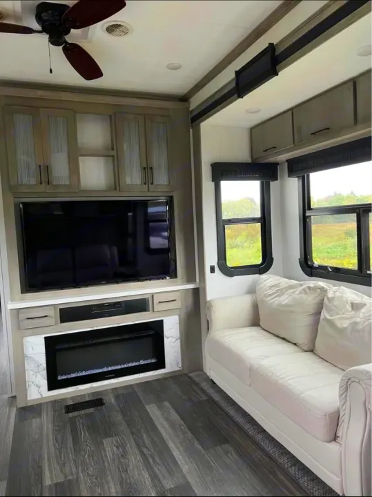 Modern RV rental living area: TV, fireplace, couch, cabinets, and ceiling fan create a comfortable space.. Heartland RVs Big Country 2021