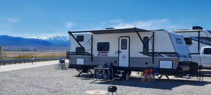 Relaxing rv rental vacation: a white Coleman travel trailer with extended awning, surrounded by camping gear, mountains in background.. Dutchmen Coleman Lantern LT 2023