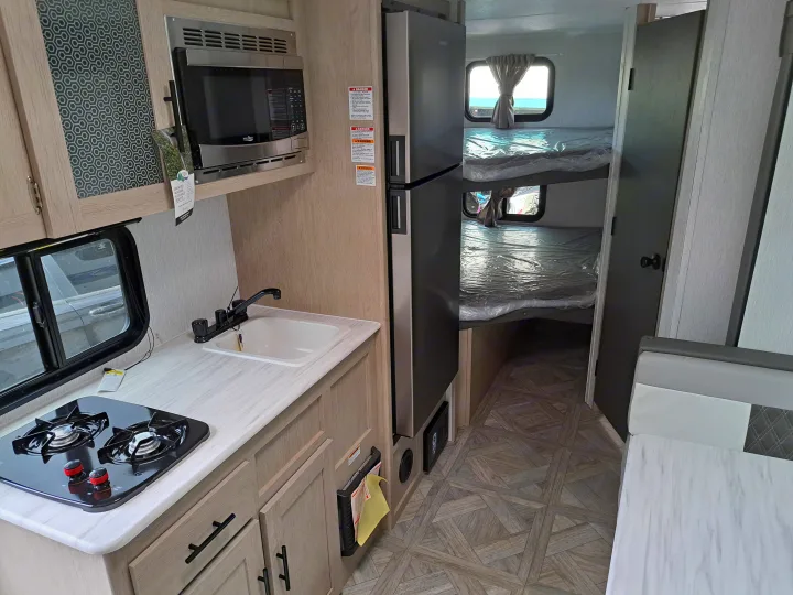 Compact RV rental interior: kitchen with microwave, stove, sink, and bunk beds with plastic covers.. Forest River Salem FSX 2024