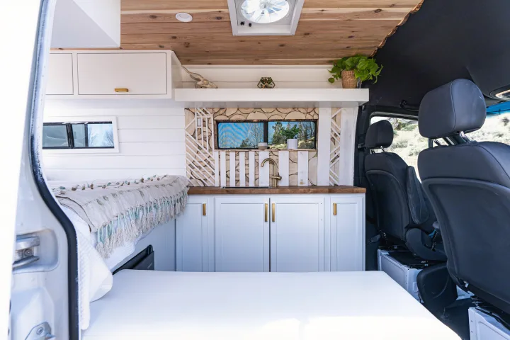 Interior of a modern camper van RV rental with a cozy bed, stylish kitchen, and natural wood accents. Perfect for travel.. Mercedes-Benz Sprinter-Loaded 2022