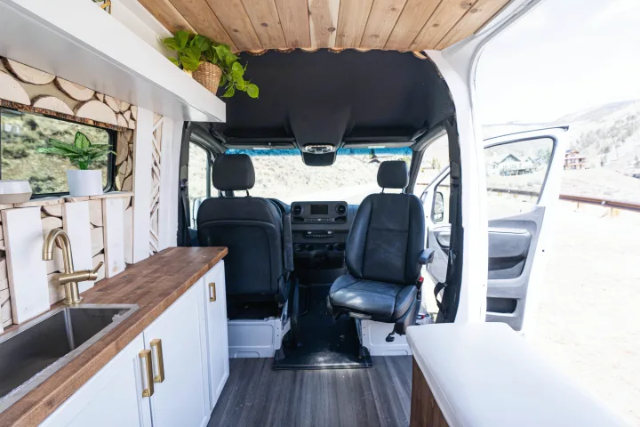 Experience comfort in this RV rental. Bright camper van interior with a modern kitchen, wood details, and mountain views.. Mercedes-Benz Sprinter-Loaded 2022