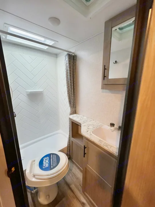 Inside an RV rental: a compact bathroom with a shower (herringbone walls), a toilet (Camping World sticker), and a vanity sink.. Dutchmen Coleman Light 2022