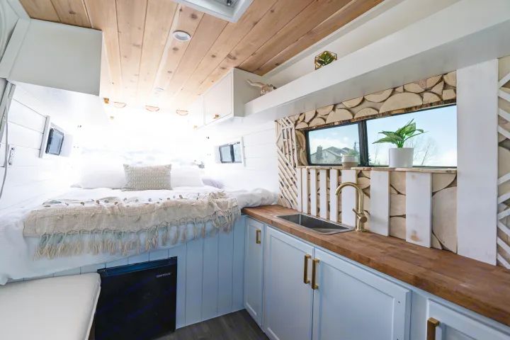 Inside a modern RV rental: comfy bed, compact kitchen with wood counters, and stylish wood wall accents.. Mercedes-Benz Sprinter-Loaded 2022