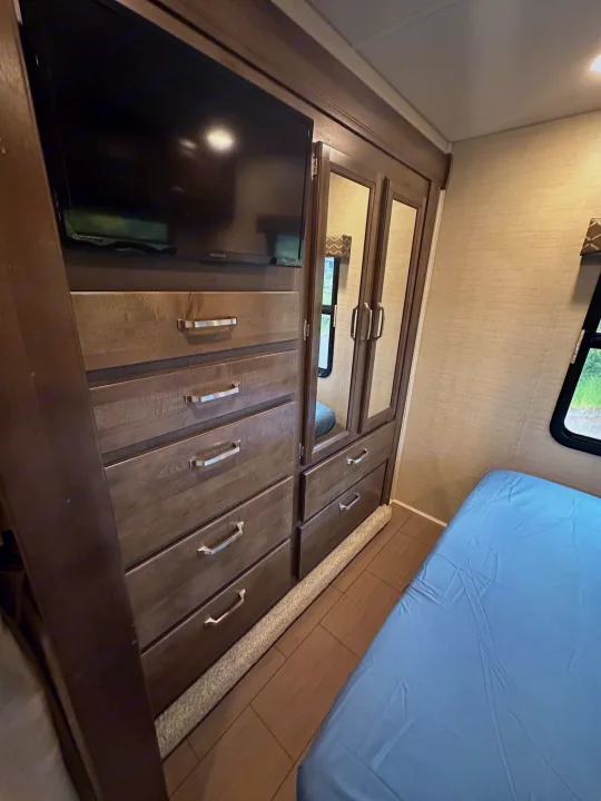 RV rental bedroom with wood dresser, TV, mirrored closet, and light blue bed.. Jayco Greyhawk 2019