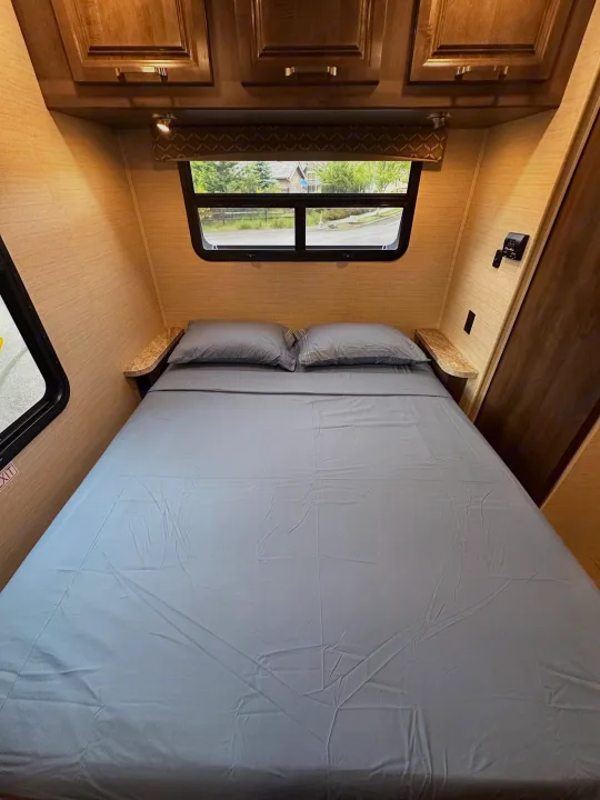 RV rental: Interior of a cozy bedroom with a bed, gray linens, overhead cabinets, and window providing natural light.. Jayco Greyhawk 2019