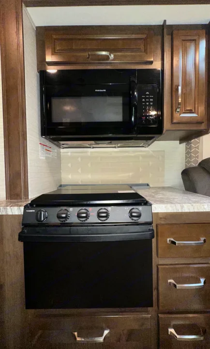 Modern RV rental kitchen showcasing a Frigidaire microwave, Dometic stove/oven, and dark wood cabinets.. Jayco Greyhawk 2019