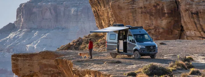 Experience an RV rental adventure! A person and dog gaze at stunning canyon views from their campervan in the desert.. Winnebago Revel 2023