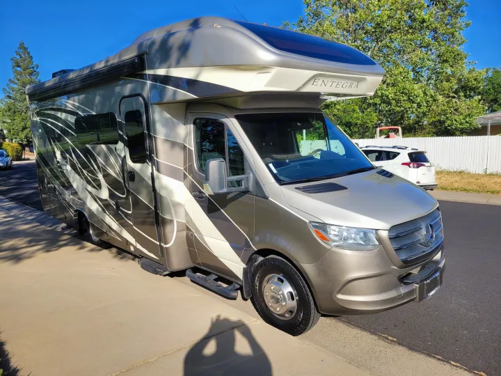 Luxurious Entegra Class C Mercedes-Benz Sprinter RV rental. Tan and grey with graphics, parked outdoors on a sunny day.. Entegra Coach Qwest 2020