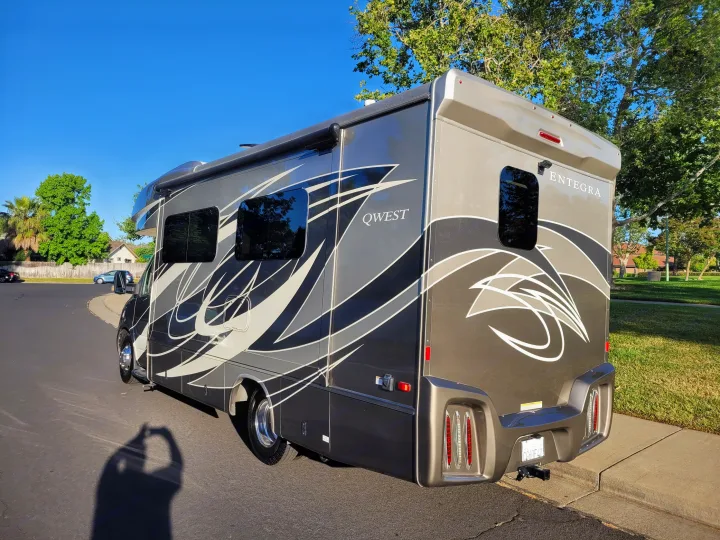 Elegant Entegra Qwest motorhome, an ideal rv rental. This large grey RV, with swirling graphics, is parked on a sunny street.. Entegra Coach Qwest 2020