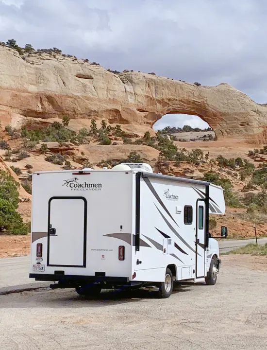 A white Coachmen Freelander RV rental parked at a scenic overlook, featuring a grand natural rock arch in a vast canyon.. Coachmen Freelander 2020