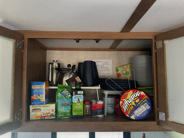 Organized RV rental kitchen cabinet with cooking essentials, teas, coffee, and dishes for a comfortable trip.. Gulf Stream Envision 2020