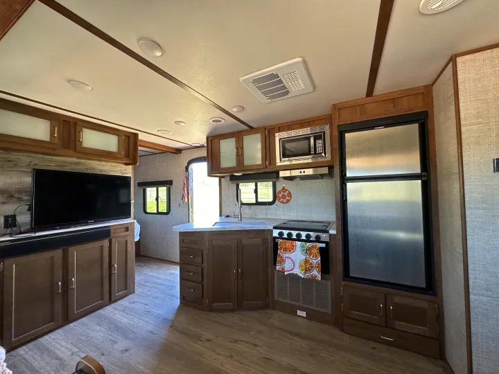 Inside this modern RV rental: a well-equipped kitchen with stove, fridge, and microwave, plus a living area with TV.. Gulf Stream Envision 2020