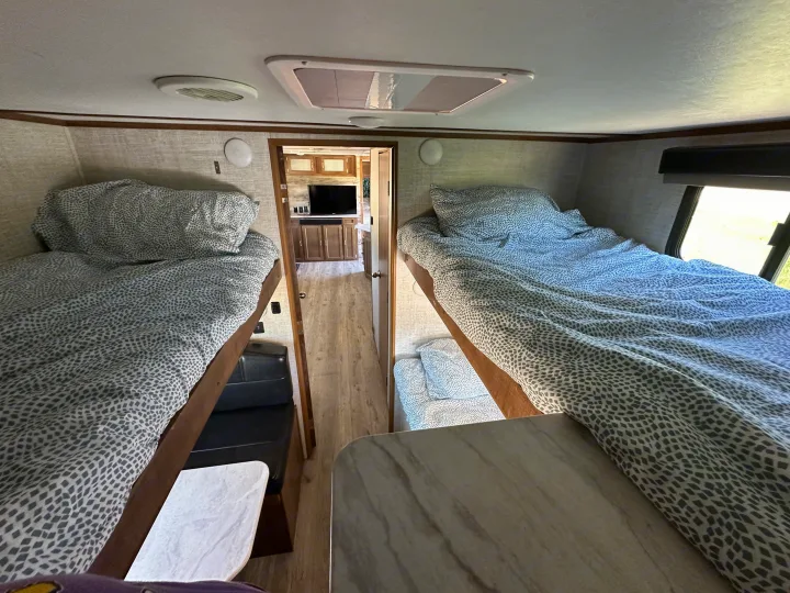 RV rental interior showing comfortable bunk beds with patterned linens, a dinette, and living space.. Gulf Stream Envision 2020