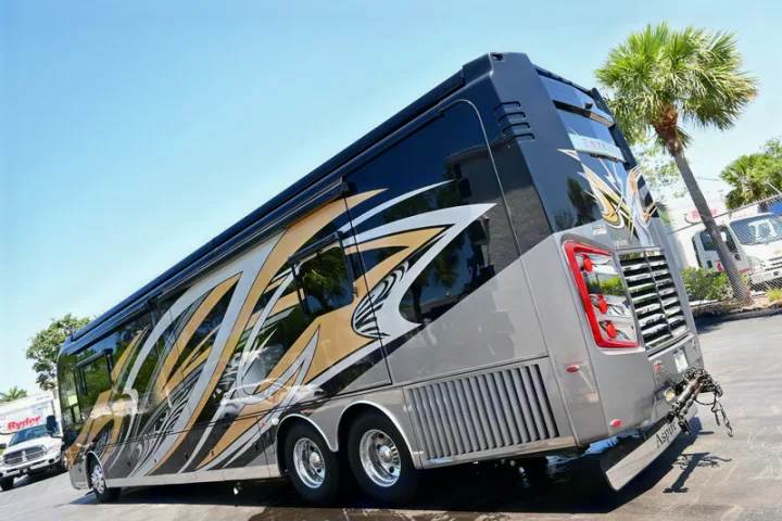 This sleek Entegra Aspire luxury RV rental, with bold black, gold, and silver graphics, is parked outdoors.. Entegra Coach Aspire 2019