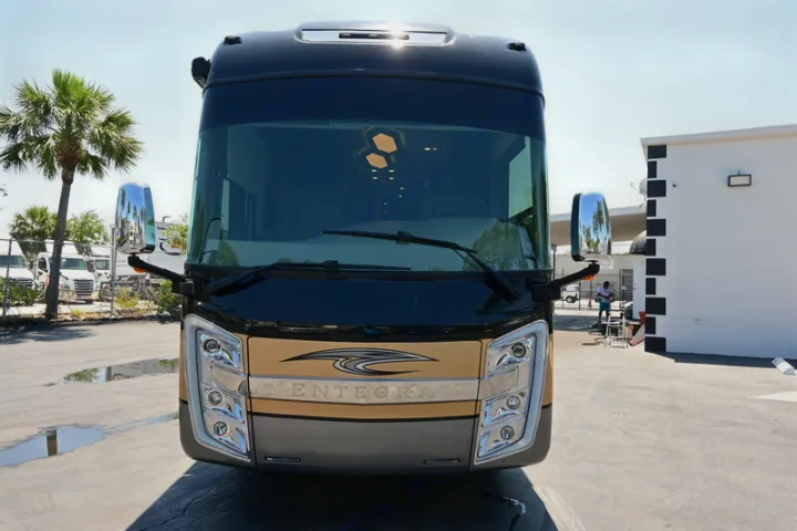 Front of a sleek, black and gold luxury RV, badged 'Entegra,' gleaming in sunlight. Ideal for an rv rental.. Entegra Coach Aspire 2019