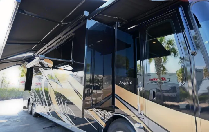 Exterior view of a black & gold Aspire luxury RV rental with side extended, awning out, ready for your road trip.. Entegra Coach Aspire 2019