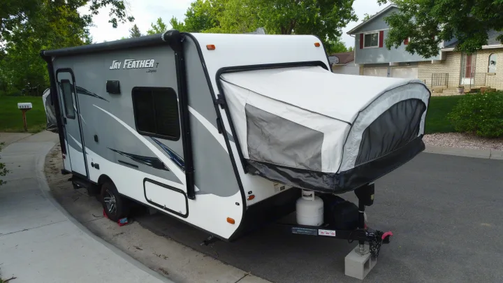 A grey and white Jay Feather pop-up travel trailer, a type of RV, parked on pavement. Perfect for an RV rental adventure!. Jayco Jay Feather 2016
