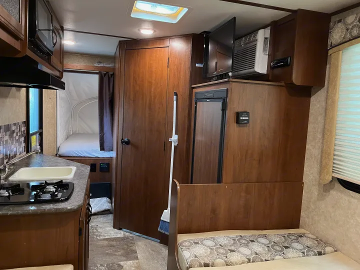 This RV rental interior showcases a functional kitchen with sink & stove, refrigerator, pop-out bed, and TV.. Jayco Jay Feather 2016