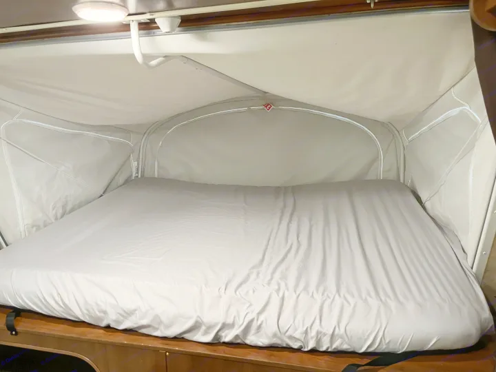 Inside a pop-up RV rental, a comfy bed with light gray sheets awaits. Perfect for your next road trip or camping adventure.. Jayco Jay Feather 2016