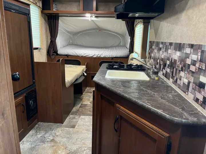 RV rental interior: A practical kitchen with a sink and stove, a cozy dining booth, and a comfortable pop-up bed.. Jayco Jay Feather 2016