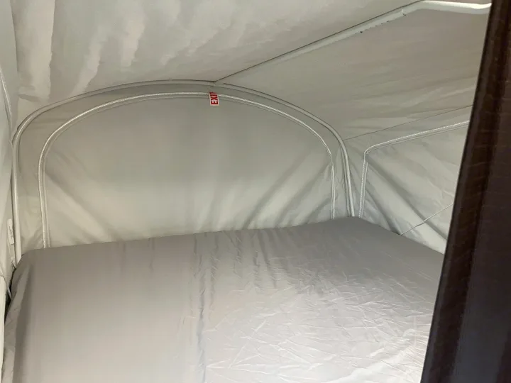 Cozy rv rental pop-up camper interior showing a light grey bed and fabric walls, with a red "EXIT" sign near the top.. Jayco Jay Feather 2016