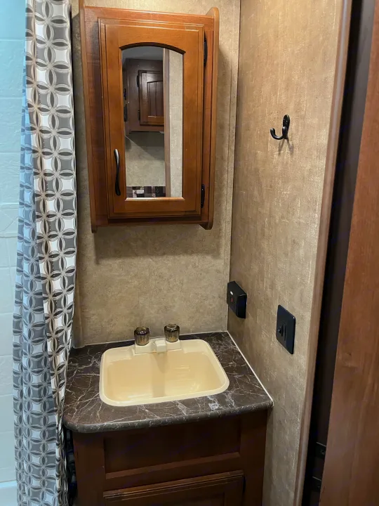 Compact RV rental bathroom: beige sink, wood vanity, mirrored cabinet, geometric shower curtain.. Jayco Jay Feather 2016