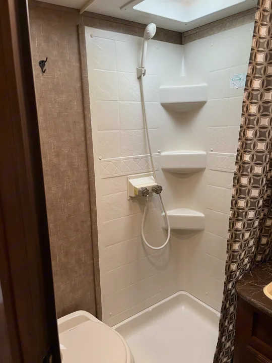 Functional RV rental bathroom with a compact shower, toilet, and patterned shower curtain.. Jayco Jay Feather 2016