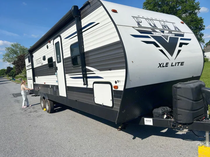 A child stands by a white Puma XLE Lite travel trailer, a great RV rental for your next adventure.. Forest River Palomino Puma XLE Lite 2021