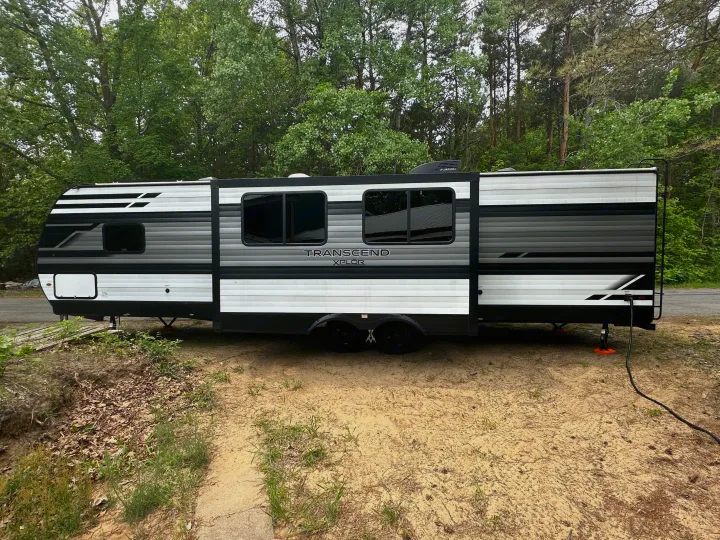 Grey Transcend XPLOR RV rental parked at a wooded campsite, ideal for outdoor adventures.. Grand Design Transcend Xplor 2022