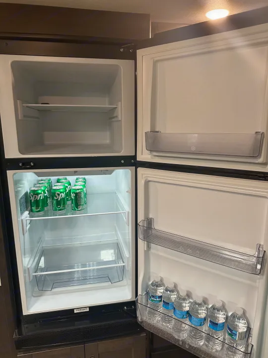 An RV rental's compact refrigerator, with an empty freezer and the fridge section stocked with Sprite and water bottles.. Grand Design Transcend Xplor 2022