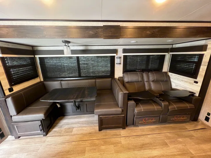 Modern RV interior featuring a U-shaped dinette, wood table, and plush reclining theater seating. Ideal for your rv rental.. Jayco White Hawk 2022