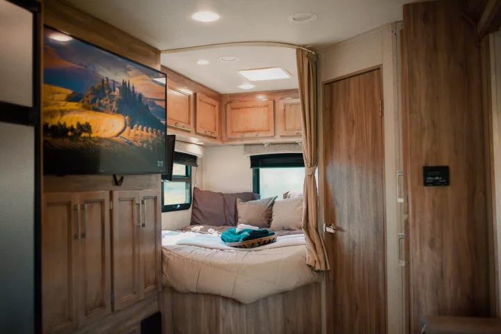 Cozy RV rental bedroom features a mounted TV, comfortable bed with fresh linens, and warm wooden interior.. Entegra Coach Odyssey 2019