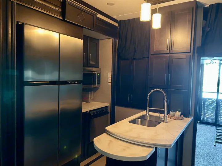 Modern RV rental kitchen with stainless steel fridge, dark cabinets, ample countertop space, and sink, ideal for travel.. Raptor Raptor 2017