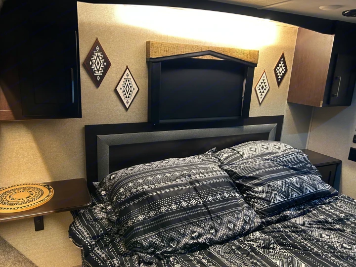 RV rental bedroom with a dark headboard, black and white tribal print bedding, floating side tables, and diamond wall decor.. Raptor Raptor 2017