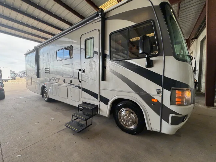 RV rental: A large white and gray motorhome parked under a metal roof, with its entrance steps open.. Forest River FR3 2016