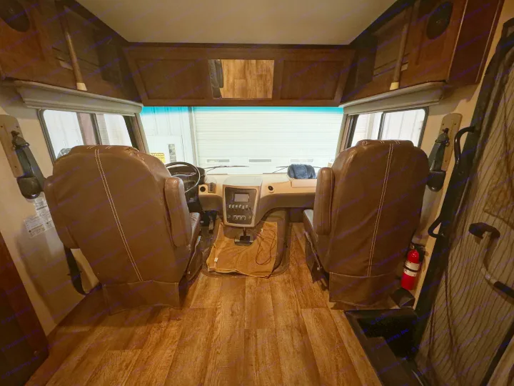 This RV rental's spacious brown-seated cockpit features a detailed dashboard and overhead storage, looking out at a garage.. Forest River FR3 2016