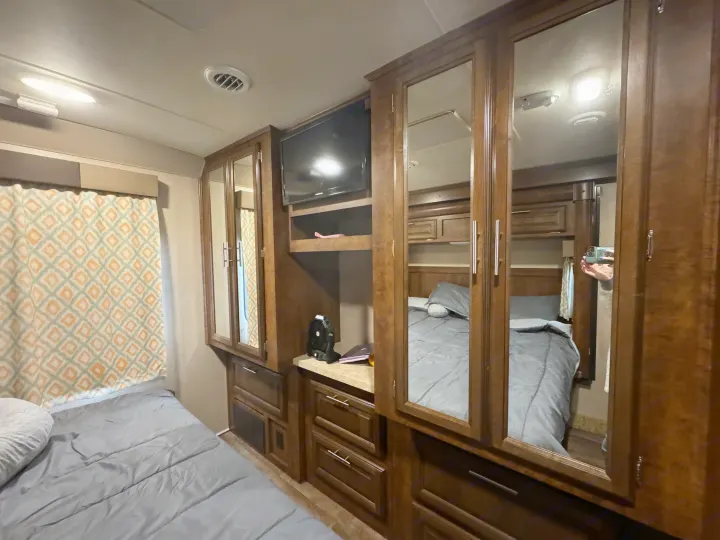 Cozy RV rental bedroom with grey bed, patterned curtains, mirrored cabinets, and TV. Ready for your next travel adventure.. Forest River FR3 2016
