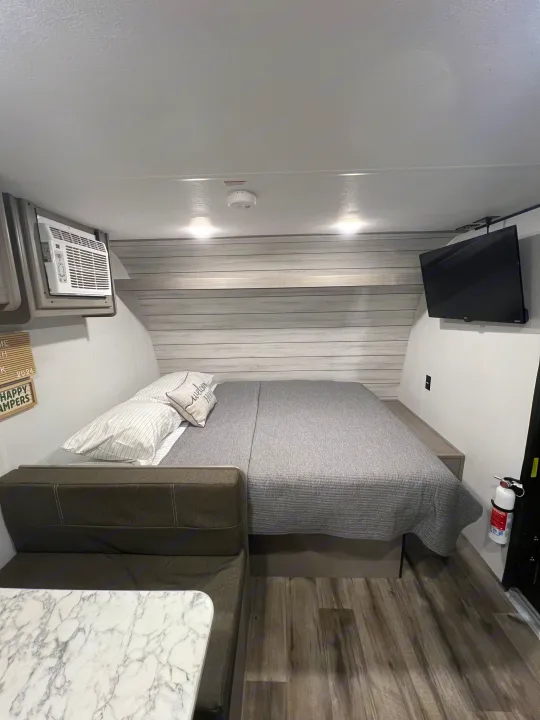 Explore this modern RV rental interior: spacious bed, seating/dinette area, AC, and TV. Perfect for your next adventure!. Coleman Lantern 17B 2024