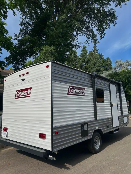 This gray and white Coleman travel trailer, ideal for an RV rental, is parked outdoors under a clear sky.. Coleman Lantern 17B 2024