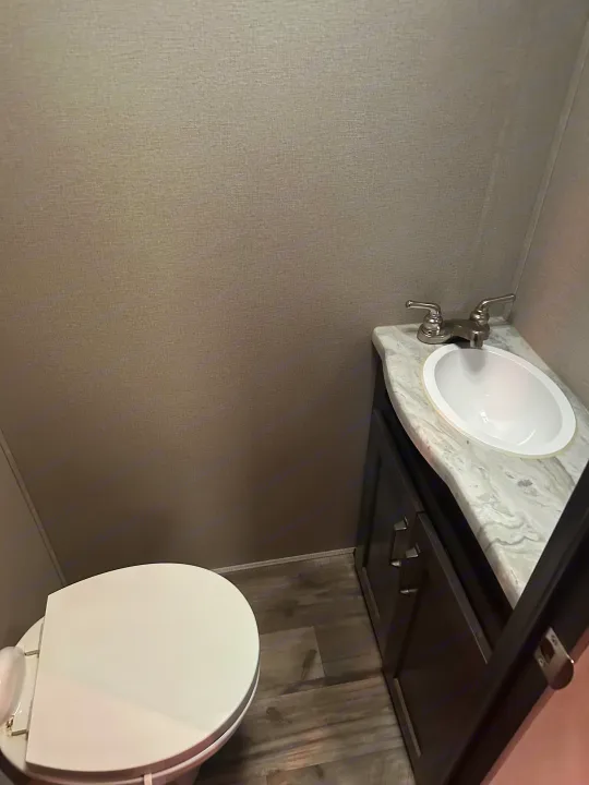 Inside an RV rental: a compact bathroom with a white toilet, dark wood vanity, and sink.. Grand Design Transcend Xplor 2022