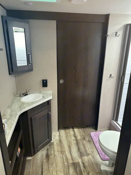 This RV rental bathroom offers a compact design with a sink, medicine cabinet, toilet, and wood grain flooring.. Grand Design Transcend Xplor 2022