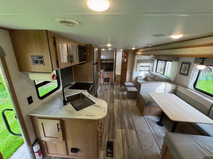 Bright RV rental interior: modern kitchen, dining/living areas, bunk beds. A clean, spacious camper.. Prime Time Avenger 2022