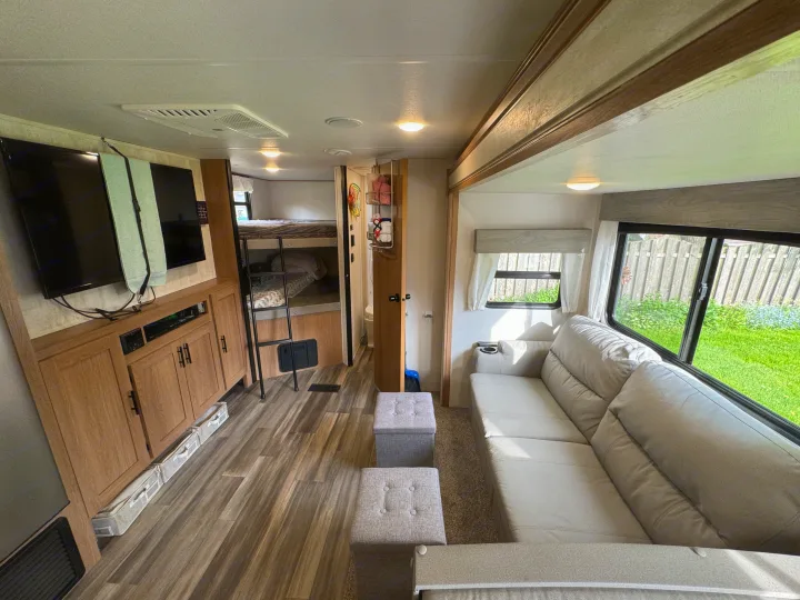 Modern RV rental interior with comfy sectional sofa, entertainment center, and bunk beds.. Prime Time Avenger 2022
