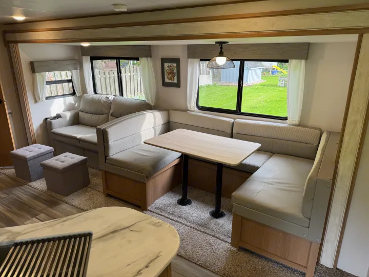 Spacious RV rental interior featuring a comfortable dinette with table, sofa, and storage ottomans in a modern living space.. Prime Time Avenger 2022