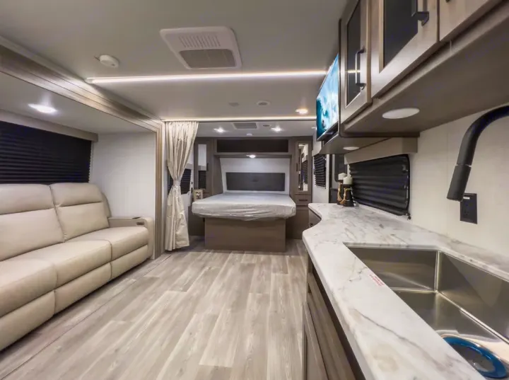 Inside a modern RV rental: Living room with sofa, private bedroom, and functional kitchen with sink.. Grand Design Transcend Xplor 2024