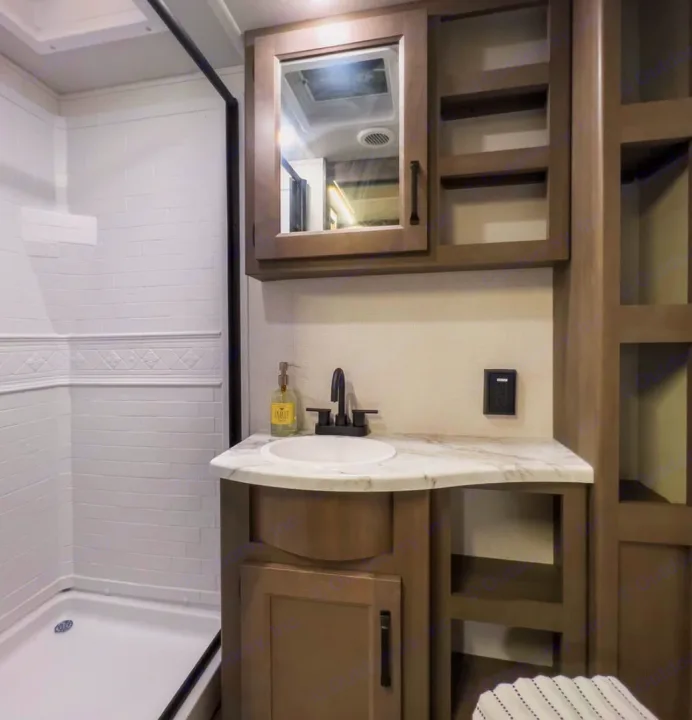 Modern RV rental bathroom with white-tiled shower, vanity, sink, and storage provides comfort on your trip.. Grand Design Transcend Xplor 2024